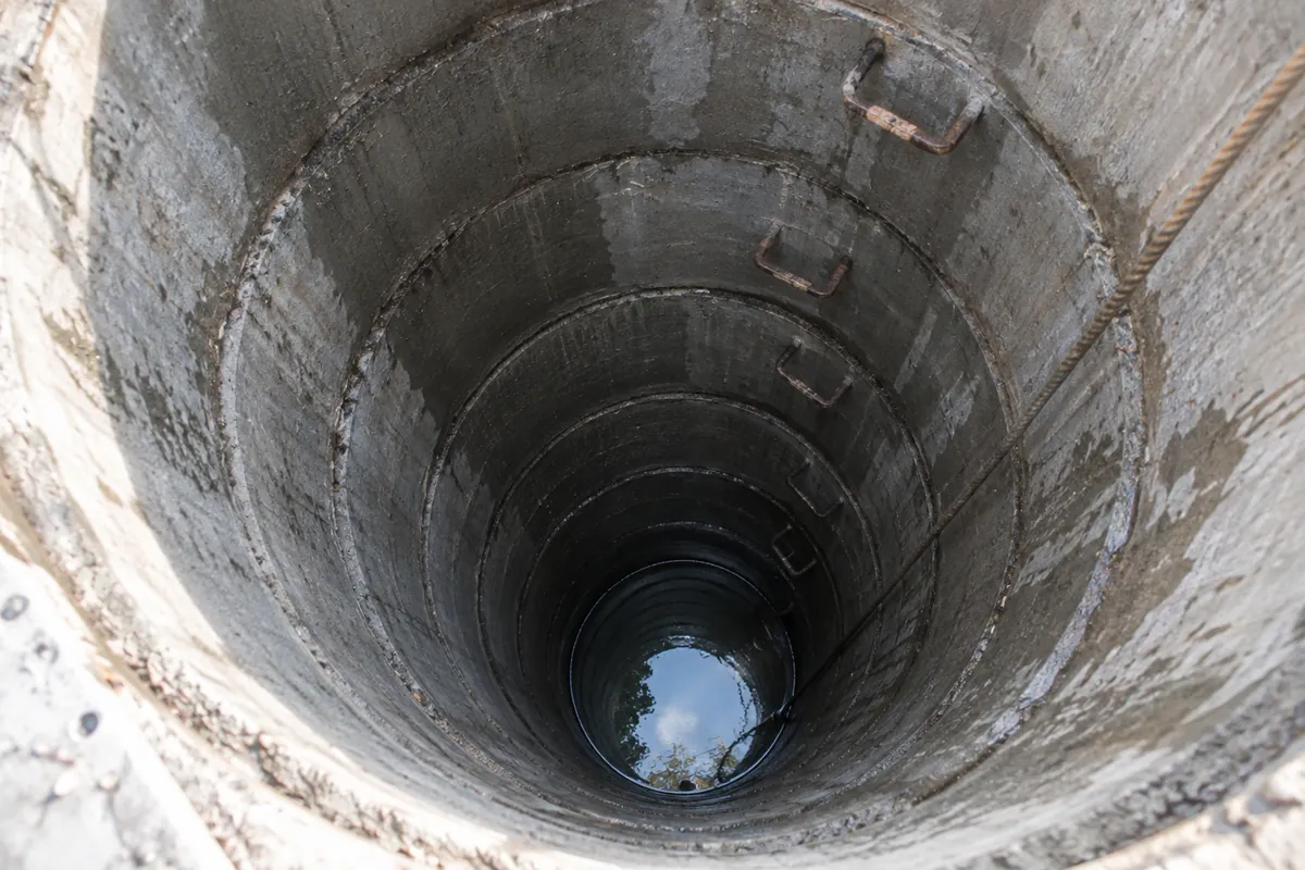 Privire de sus într-o fântână curată din inele de beton, cu apă limpede pe fund